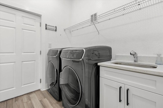 laundry room with light wood-type flooring, sink, washing machine and clothes dryer, and cabinets