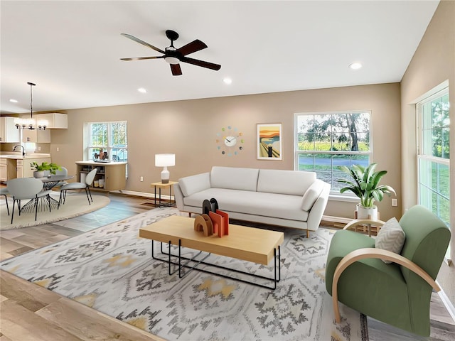 living room with a healthy amount of sunlight, light wood-type flooring, sink, and ceiling fan with notable chandelier