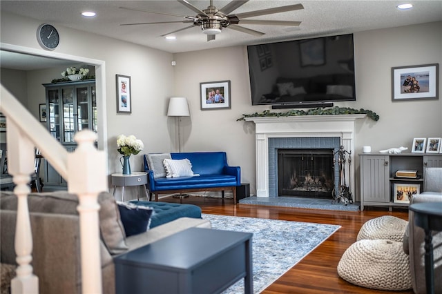 living room featuring a textured ceiling, a brick fireplace, hardwood / wood-style floors, and ceiling fan