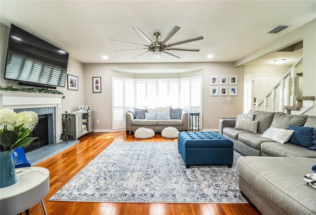 living room with ceiling fan, a fireplace, a textured ceiling, and light hardwood / wood-style flooring