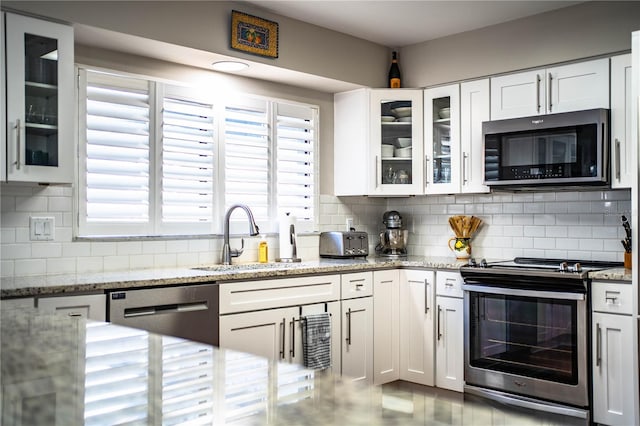 kitchen featuring light stone countertops, stainless steel appliances, white cabinetry, and sink