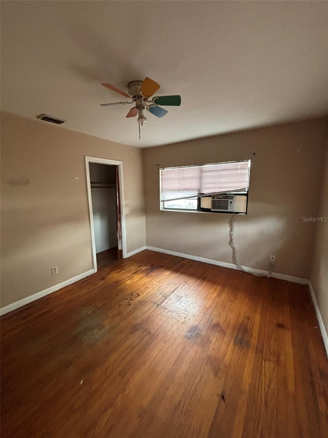 unfurnished bedroom with ceiling fan, a walk in closet, a closet, and dark wood-type flooring