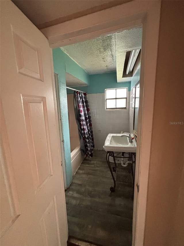 bathroom with a textured ceiling, shower / bathtub combination with curtain, hardwood / wood-style flooring, and sink