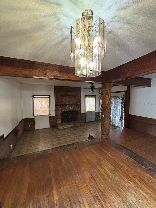 unfurnished living room featuring ceiling fan with notable chandelier, a textured ceiling, ornate columns, a stone fireplace, and hardwood / wood-style flooring