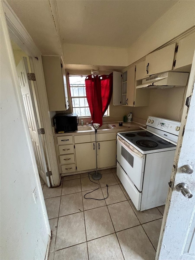 kitchen with sink, electric range, light tile patterned floors, and cream cabinets