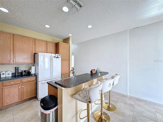 kitchen with light tile patterned flooring, a breakfast bar area, white refrigerator, and a textured ceiling