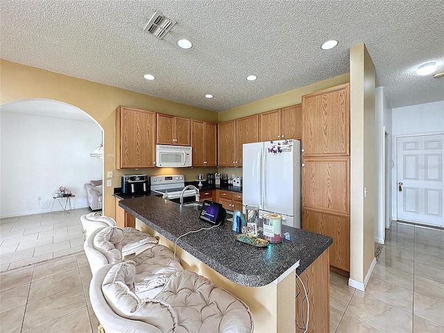 kitchen featuring light tile patterned floors, a center island with sink, white appliances, a kitchen breakfast bar, and a textured ceiling