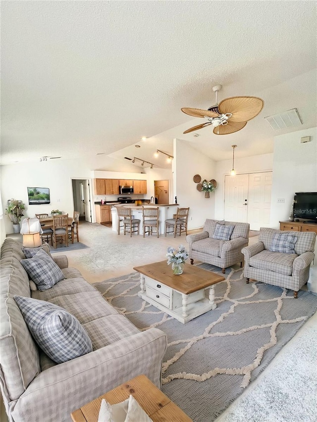 living room featuring ceiling fan, lofted ceiling, carpet floors, and a textured ceiling