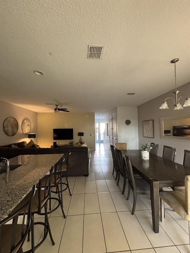 tiled dining area with sink, ceiling fan with notable chandelier, and a textured ceiling