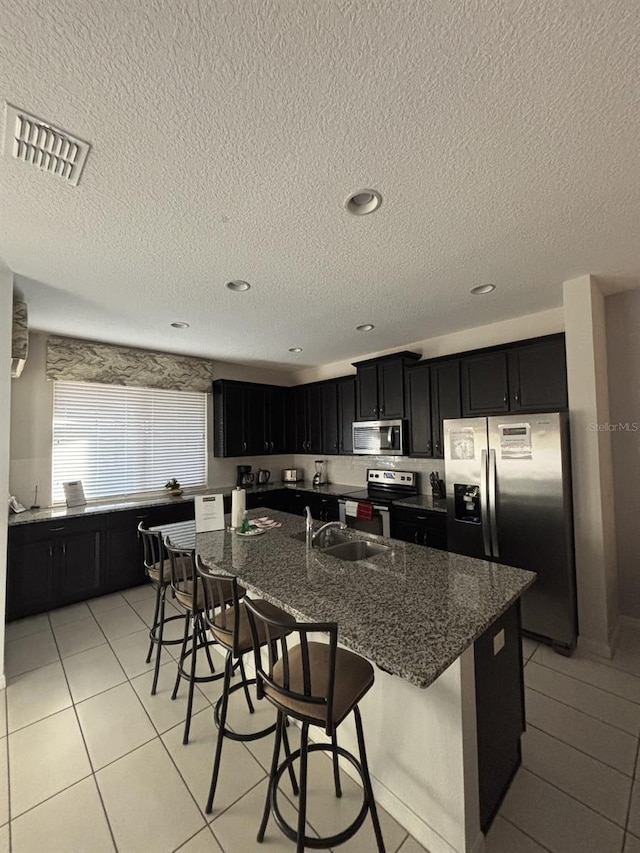 kitchen with a center island with sink, stainless steel appliances, a breakfast bar area, and dark stone countertops