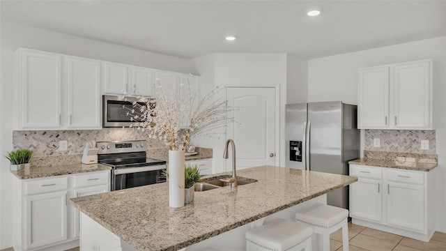 kitchen with light tile patterned flooring, sink, white cabinetry, a center island with sink, and stainless steel appliances