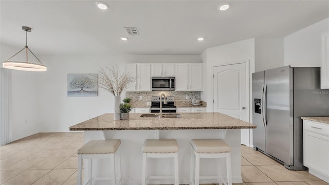 kitchen featuring light tile patterned floors, appliances with stainless steel finishes, light stone countertops, white cabinets, and a center island with sink