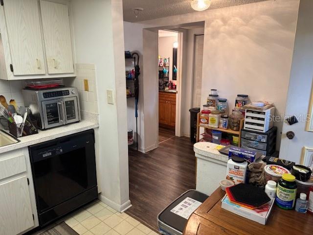 kitchen featuring tasteful backsplash, light tile patterned flooring, black dishwasher, and a textured ceiling