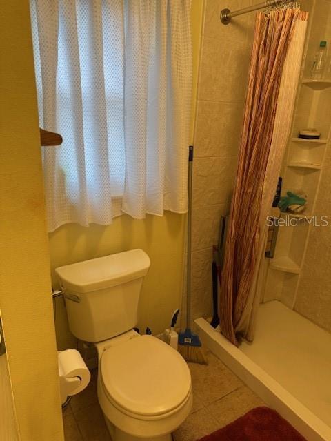 bathroom featuring toilet, tile patterned floors, and a shower with shower curtain