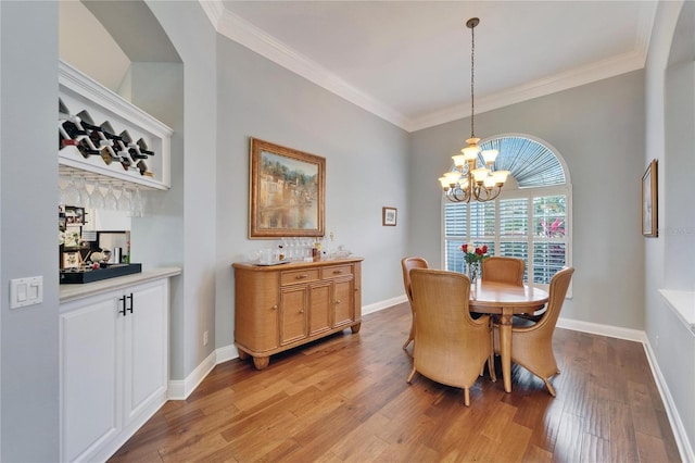 dining space featuring light wood-type flooring, a chandelier, bar area, and ornamental molding