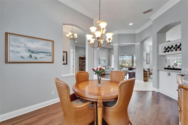 dining room featuring crown molding, light wood-type flooring, a chandelier, and ornate columns