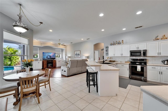 kitchen with a kitchen bar, appliances with stainless steel finishes, tasteful backsplash, white cabinetry, and light tile patterned flooring