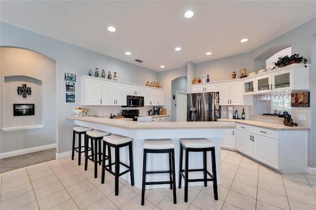 kitchen with white cabinetry, decorative backsplash, a kitchen breakfast bar, electric range, and stainless steel fridge