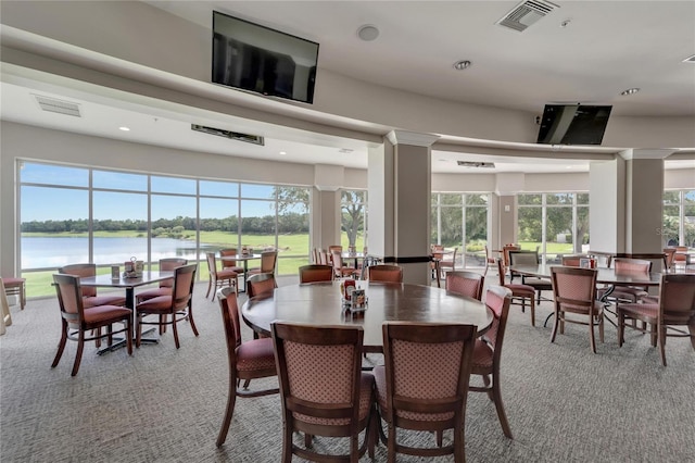 dining area featuring light carpet, a water view, and ornate columns