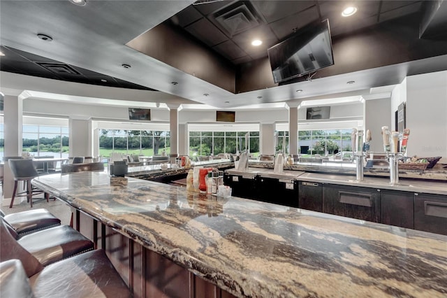 kitchen with decorative columns, light stone countertops, a kitchen breakfast bar, and dark brown cabinets