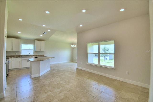 kitchen with a chandelier, light stone countertops, a kitchen island, white cabinets, and sink