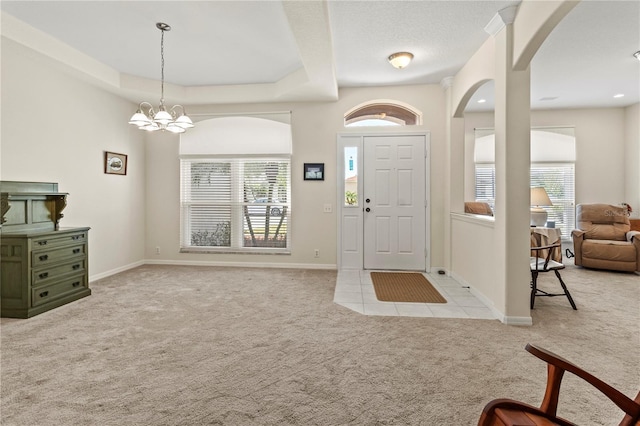 carpeted entrance foyer featuring a tray ceiling, a chandelier, and a healthy amount of sunlight