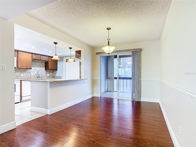 kitchen with white appliances, decorative light fixtures, wood-type flooring, backsplash, and kitchen peninsula