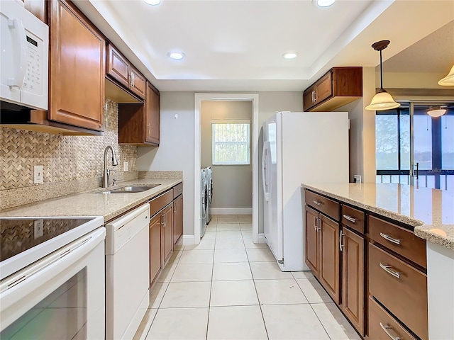 kitchen with light stone countertops, white appliances, washer and clothes dryer, decorative light fixtures, and sink