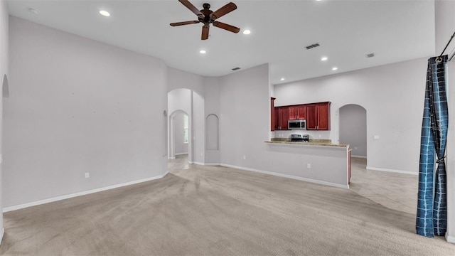 unfurnished living room with ceiling fan, light colored carpet, and a towering ceiling