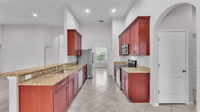 kitchen featuring appliances with stainless steel finishes, kitchen peninsula, light stone counters, and sink