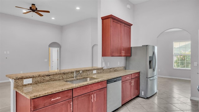 kitchen featuring kitchen peninsula, ceiling fan, stainless steel appliances, light stone counters, and sink