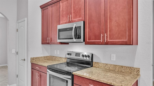 kitchen with light tile patterned floors, stainless steel appliances, and light stone counters