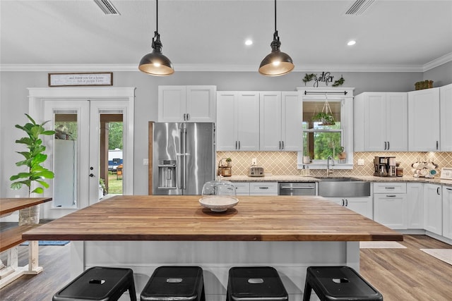 kitchen with wood counters, stainless steel appliances, pendant lighting, and white cabinetry