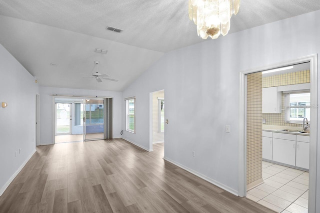 spare room featuring lofted ceiling, sink, a textured ceiling, ceiling fan with notable chandelier, and light wood-type flooring