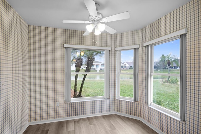 unfurnished sunroom with ceiling fan and a water view