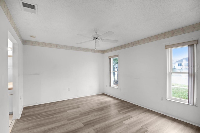 spare room featuring ceiling fan, a healthy amount of sunlight, a textured ceiling, and light wood-type flooring