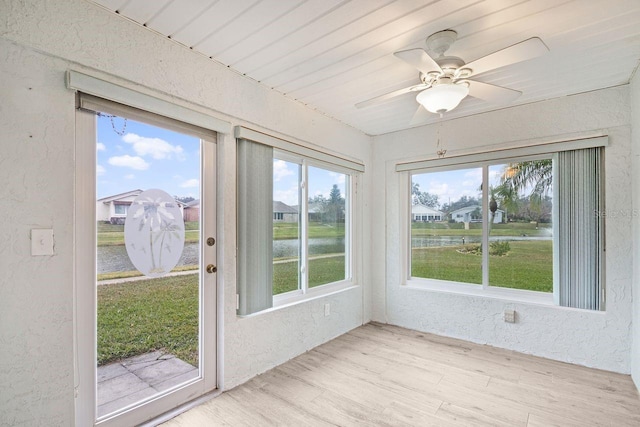 unfurnished sunroom with ceiling fan and a water view