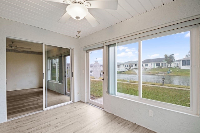 unfurnished sunroom with wood ceiling, ceiling fan, and a water view