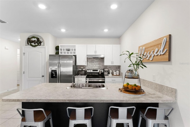 kitchen featuring a breakfast bar, light tile patterned floors, appliances with stainless steel finishes, decorative backsplash, and white cabinets