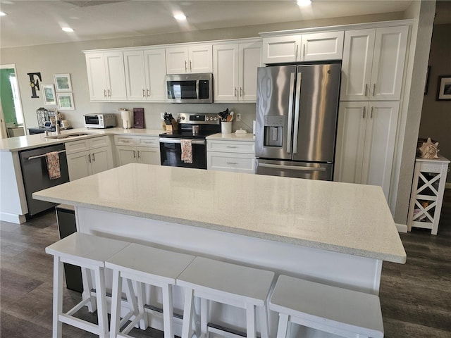 kitchen with appliances with stainless steel finishes, a kitchen island, white cabinetry, dark hardwood / wood-style flooring, and a breakfast bar