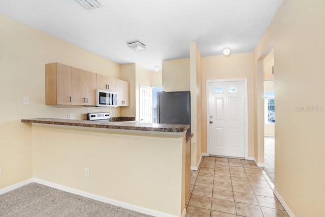 kitchen featuring kitchen peninsula, stainless steel refrigerator, light tile patterned floors, light brown cabinetry, and range