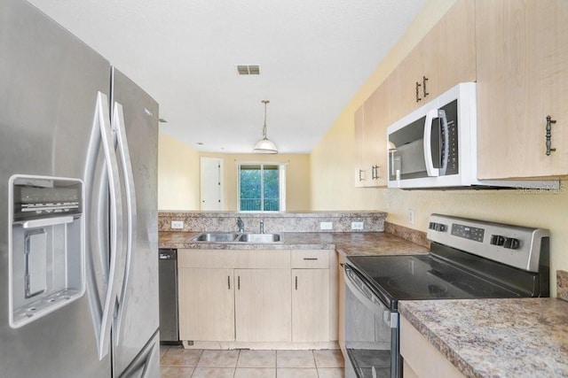 kitchen featuring appliances with stainless steel finishes, light brown cabinetry, sink, hanging light fixtures, and light tile patterned floors