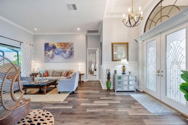 entrance foyer with hardwood / wood-style floors, crown molding, a notable chandelier, and french doors