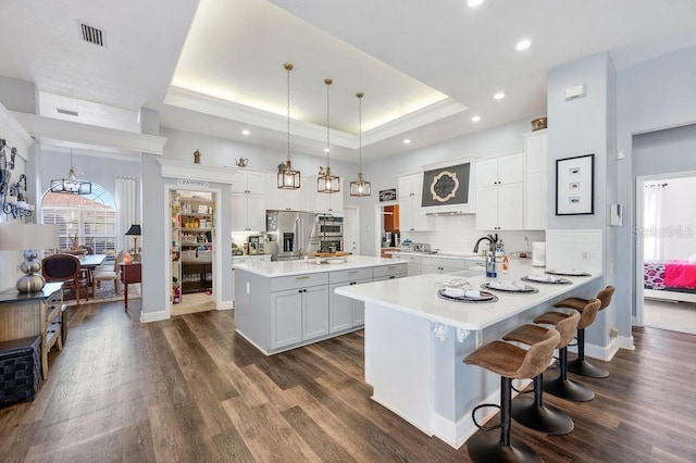 kitchen with white cabinetry, high quality fridge, a raised ceiling, kitchen peninsula, and pendant lighting