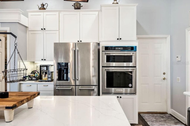 kitchen with light stone countertops, appliances with stainless steel finishes, white cabinets, and decorative backsplash