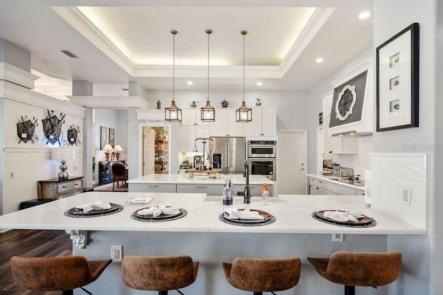 kitchen with appliances with stainless steel finishes, decorative light fixtures, decorative backsplash, a large island with sink, and a raised ceiling