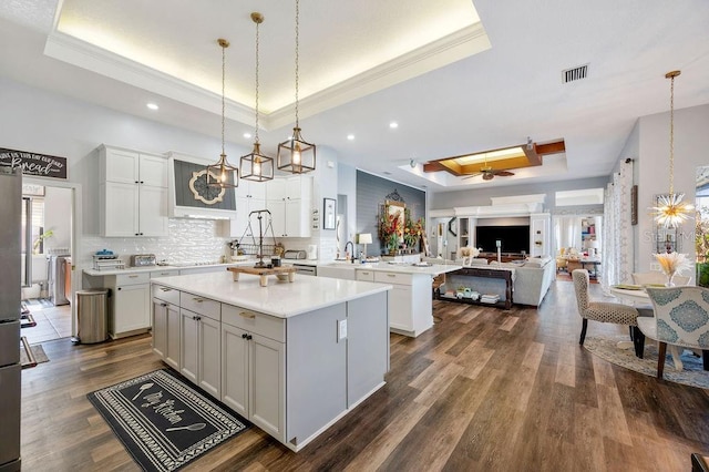 kitchen with decorative light fixtures, a tray ceiling, kitchen peninsula, a kitchen island, and backsplash