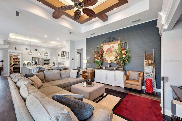 living room featuring ceiling fan, a high ceiling, a tray ceiling, dark hardwood / wood-style flooring, and wood walls