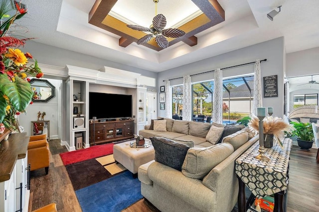 living room with dark hardwood / wood-style flooring, a tray ceiling, and ceiling fan