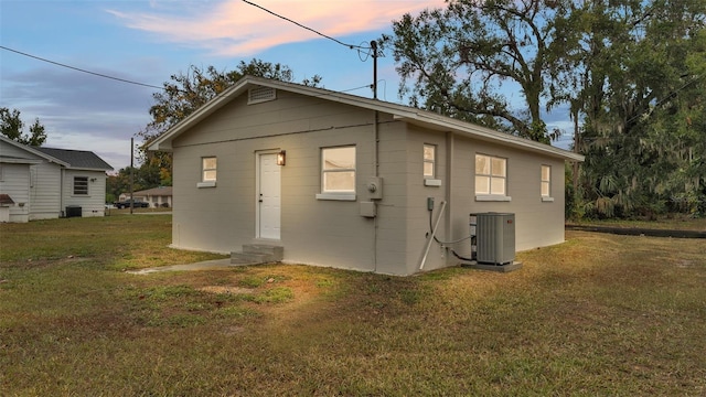 back house at dusk featuring a lawn and central AC